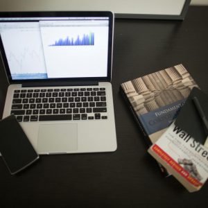 Top view of a desk with laptop, charts, books, and coffee, depicting a modern financial workspace setup.